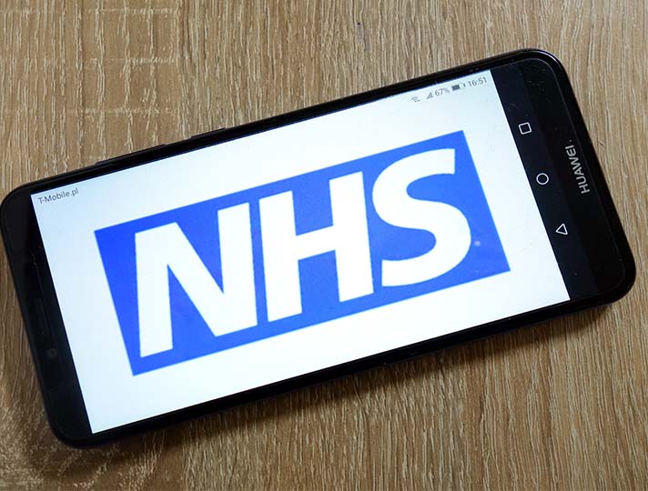 NHS logo on phone screen laying on wooden table